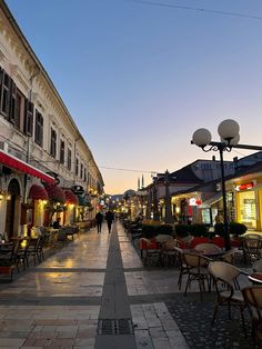 an empty street with tables and chairs on the side walk in front of some buildings