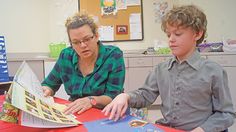 a woman and boy are sitting at a table looking at an open book with pictures on it