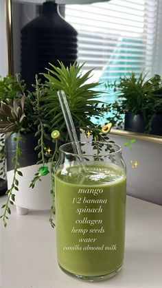 a green smoothie in a glass with a straw on the side and some plants behind it