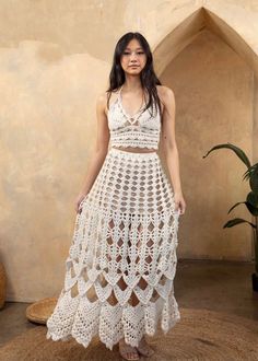 a woman in a white crochet dress standing on a rug with her hands behind her back