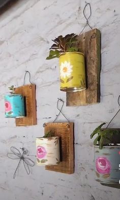 three tin cans are hanging on the wall with some plants in them and one is holding a planter