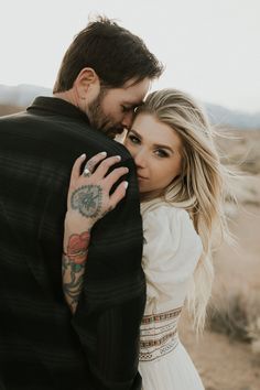 a man and woman embracing each other with tattoos on their arms, in the desert