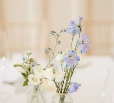 two vases filled with flowers on top of a white table cloth covered dining room table