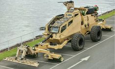 an armored vehicle parked in a parking lot next to the water and grass near by