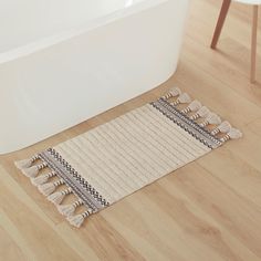 a bath tub sitting next to a rug with tassels on it in a bathroom