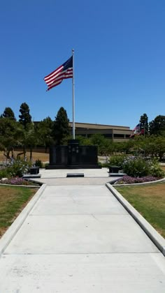 an american flag is flying at half mast in front of a memorial with flowers and trees