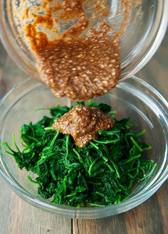 two bowls filled with greens and sauce on top of a wooden table