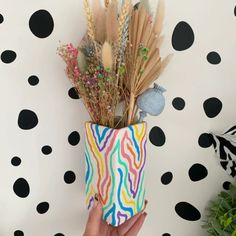 a hand holding up a vase with flowers and feathers in it against a polka dot wall