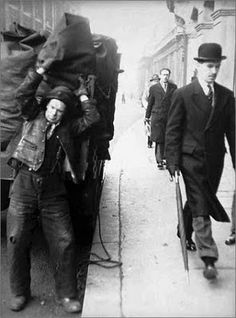 an old black and white photo of men walking down the street with luggage on their back