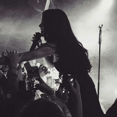 the woman is holding up her cell phone while she sings to someone else on stage