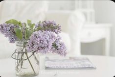 purple flowers in a mason jar sitting on a white coffee table next to a couch