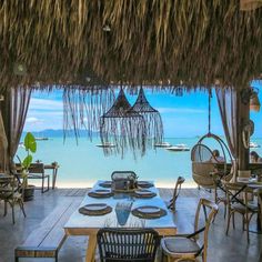 an outdoor dining area overlooking the ocean with wicker chairs and rattan hanging from the roof