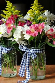 two mason jars filled with colorful flowers sitting on a wooden table next to each other