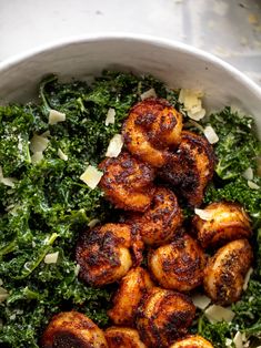 a white bowl filled with cooked shrimp and greens