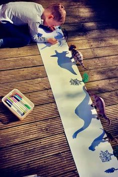 a young boy is painting on a long paper with animals and trees in the background