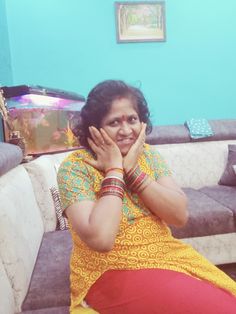 a woman sitting on top of a couch in front of a blue wall and holding her hands to her face