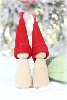 two wooden pegs with red felt hats on top of them next to a christmas tree