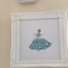 a white frame with a blue dress on it next to a cell phone charger