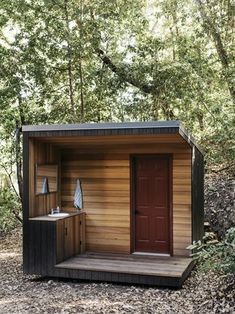 a small wooden cabin in the woods with a red door and two sinks on it