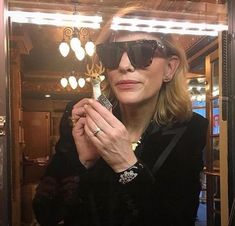 a woman wearing sunglasses is holding a cell phone in front of a mirror with lights