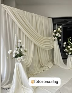 a white wedding ceremony with flowers on the floor and drapes draped over it's head