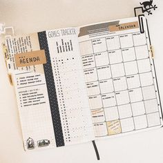 an open planner is sitting on top of a white table with black and gold accents