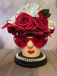 a red and white flower arrangement in a mannequin's head on a wooden table