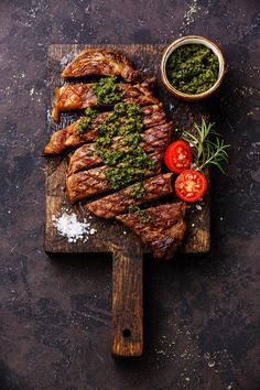 grilled steak with pesto and tomatoes on wooden cutting board next to small bowl