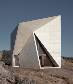 the building is made out of concrete and sits on top of a rocky hill in front of