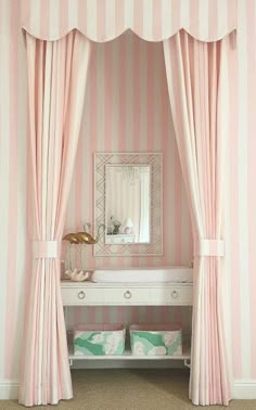 a bedroom with pink and white striped walls, curtains and a dressing table in front of a mirror