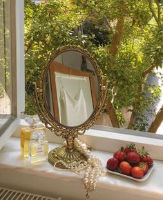 a mirror sitting on top of a window sill next to strawberries and a bottle