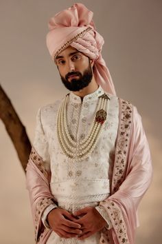 Gardenia Pink Sherwani Set | Jatin Malik Introducing our exquisite white all-over hand-embroidered sherwani set, a true masterpiece of craftsmanship and elegance. The foundation of this ensemble is meticulously crafted using tone-on-tone thread, creating a subtle and sophisticated base texture. Adorned with delicate silver zari work throughout, the sherwani exudes an air of refinement and luxury. Paired with a baby pink hand-embroidered stole and safa, this ensemble strikes a perfect balance between tradition and modernity, making it an ideal choice for weddings and special occasions. Included in purchase: Sherwani, Kurta, Churidar, Stole, Safa, Cummerbund Product Specification Color: White Fabric: Linen silk Occasion: Engagement, Wedding, Bridal, Reception Style: Sherwani, Kurta, Churidar Designer Luxury Off White Sherwani, Luxury Georgette Sherwani With Intricate Embroidery, Luxury Designer Off White Sherwani, Luxury Pink Sherwani For Transitional Season, Pink Sherwani, White Sherwani, Jatin Malik, Wedding Suit Ideas, Blouse Yoke