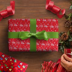 a person holding a wrapped present on top of a wooden table next to christmas decorations