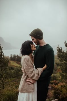 a man and woman standing next to each other in front of some trees on a foggy day