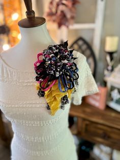 a white dress with black, yellow and red flowers on the front is sitting on a mannequin