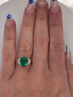 a woman's hand with blue and white nail polish holding an emerald ring on her finger