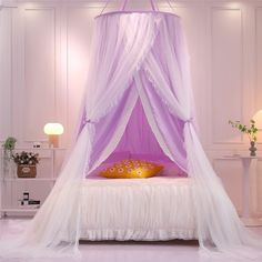 a white bed with a purple canopy and pillows on top of it in a room