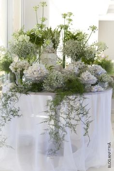 a table topped with white flowers and greenery on top of a cloth covered table