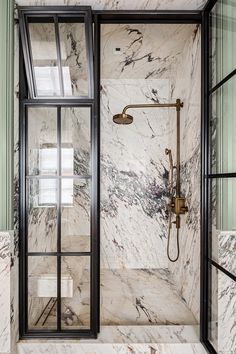 a bathroom with green walls and marble flooring, glass shower enclosures and black framed windows