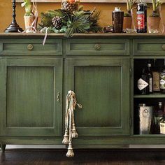 an old green cabinet with lots of bottles and plants on it's top shelf