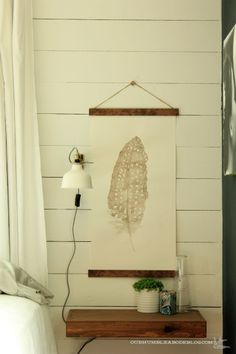 a white bed room with a painting on the wall next to a night stand and lamp