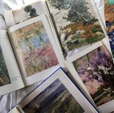 an open book with pictures of trees and flowers on it sitting on a bed next to other books