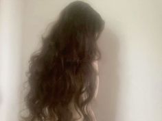 the back of a woman's head with long, curly hair in front of a white wall