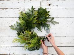 a person is making a wreath out of branches on a white wooden background with wood planks