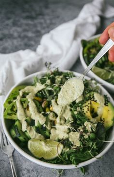 a person holding a fork in a bowl filled with vegetables and sauces on the side