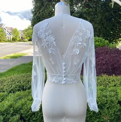 the back of a white dress on display in front of some bushes and grass with houses in the background