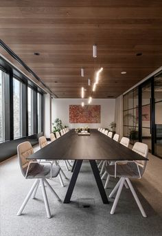 a long table with chairs around it in front of large windowed walls and floor to ceiling windows