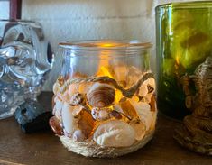 two glass jars filled with seashells on top of a wooden table next to an elephant figurine