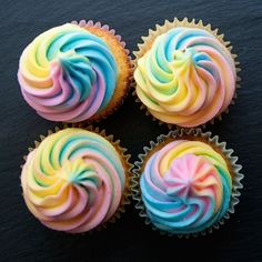 four cupcakes with different colored frosting on top of each one, sitting on a black surface