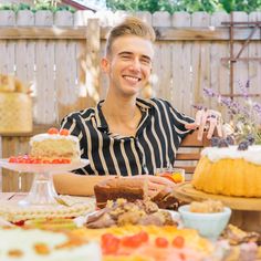 a young man sitting at a table with cake and other desserts on the table